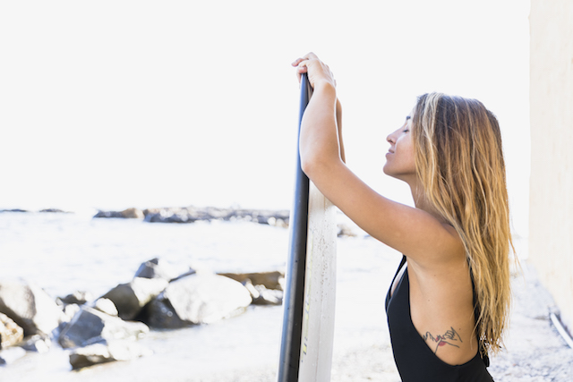 woman with surfboard, showing her side tattoo.