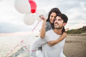Couple together at beach on a date with girl holding balloons