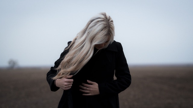 woman wearing black, face is covered by hair, looking somber.