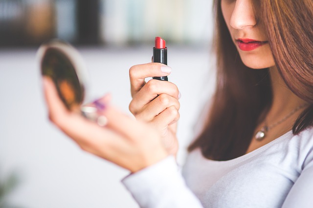 woman looking into a compact applying lipstick.