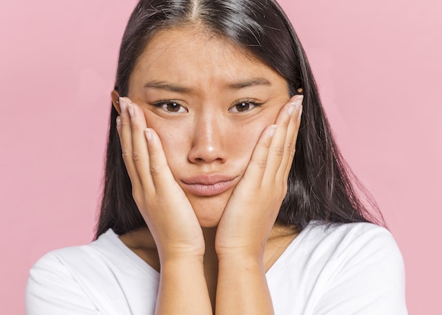 a woman holding her face looking worries, has some wrinkles. 