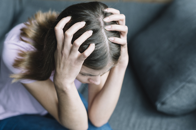 woman holding head, scalp with hair thinning showing.