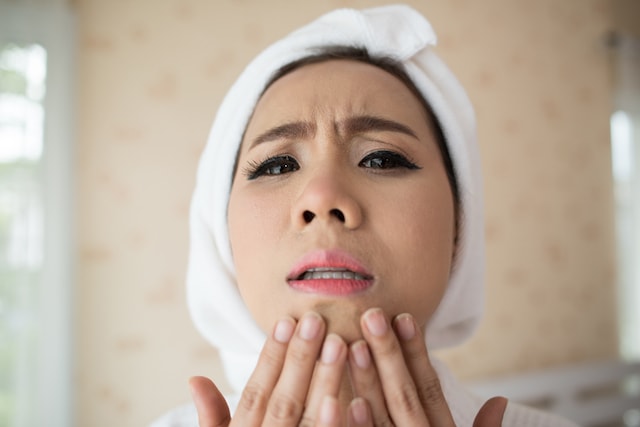 women looking at camera as if it were a mirror, touching her acne on her chin.