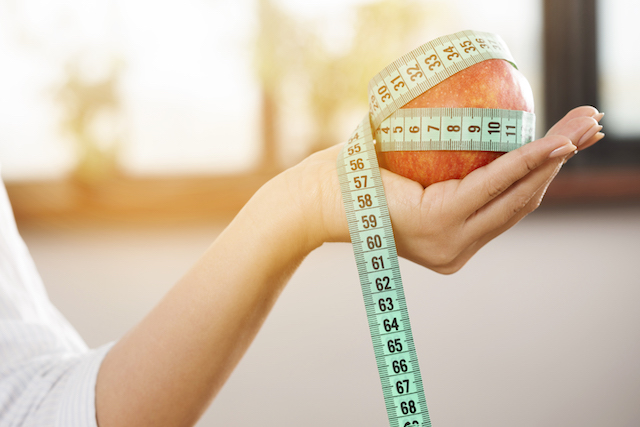 woman holding apple wrapped in measuring tape. 