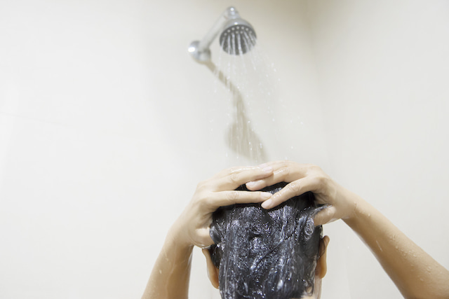person washing hair in the shower under shower head.