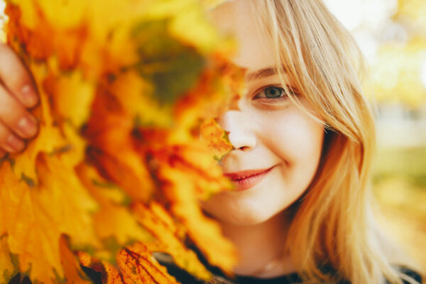 a woman smiling holding fall leaves to cover half of her face