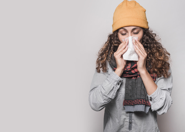 a woman sneezing wearing fall clothes. 