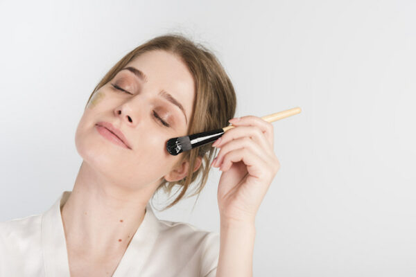 woman applying concealer with a brush on her face.
