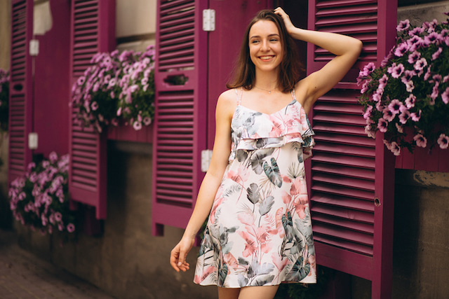 woman smiling wearing a floral dress and surrounded by flowers. 